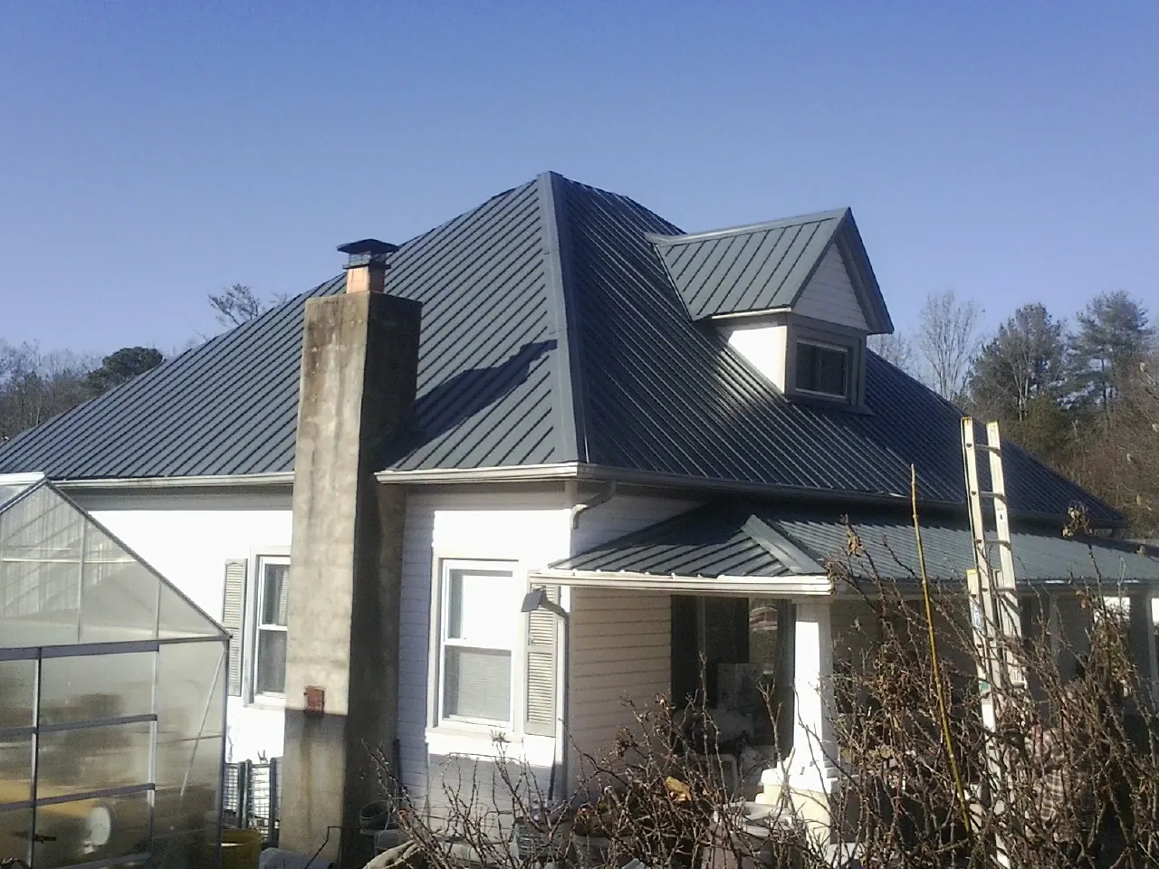 Dark blue standing seam metal roof on a white farmhouse with dormer — Slate & Tile Roof Repair by Roofing Brothers in Prairie Lea