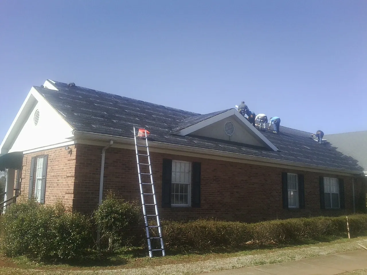 Crew tearing shingles off a brick ranch roof with a ladder set — Emergency Roof Repair work by our crew in Prairie Lea