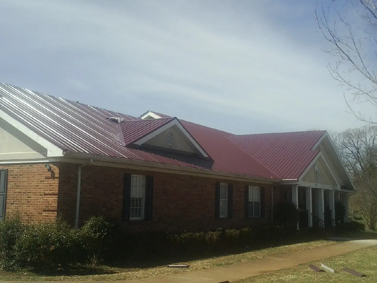 Red metal roof with gabled entries on a long brick building, from a Hail Damage Roof Repair job in Prairie Lea