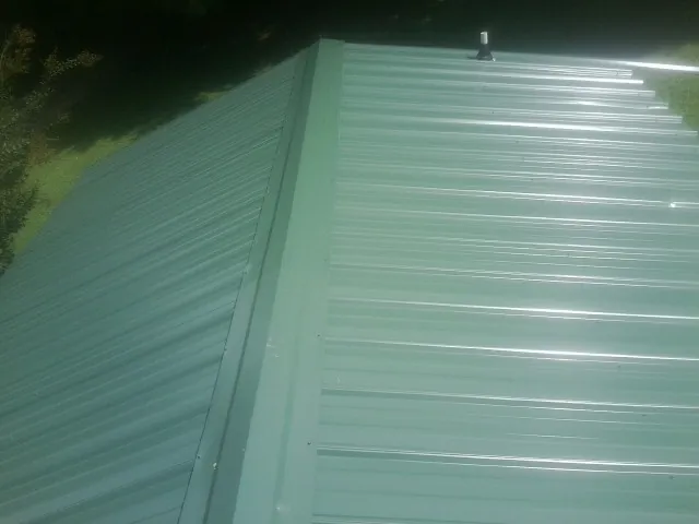New green metal panels meeting at the ridge of a roof — Flat Roof Repair work by our crew in Prairie Lea