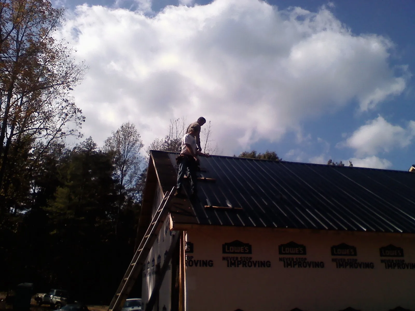 Roofer fastening dark metal panels high against a cloudy sky, from a Roof Inspection job in Prairie Lea