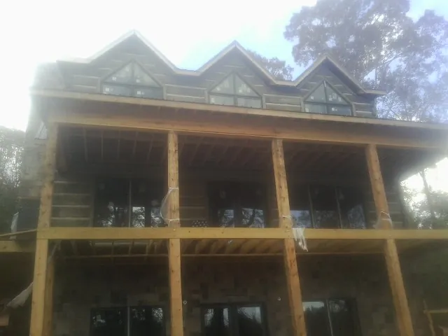 Dormers and porch framing on a large log home under construction — Roof Coating work by our crew in Prairie Lea