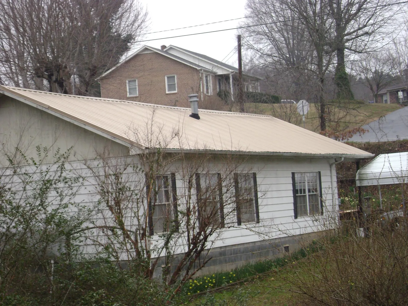 Tan metal roof on a white sided house set into a hillside — Commercial Roofing by Roofing Brothers in Prairie Lea