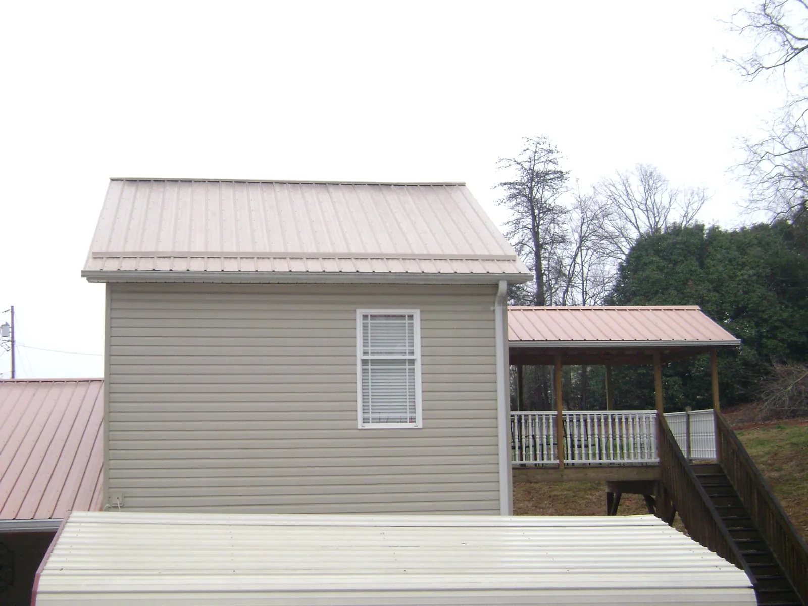 Tan metal roofs on a two story addition and attached porch, from a Roof Replacement job in Prairie Lea